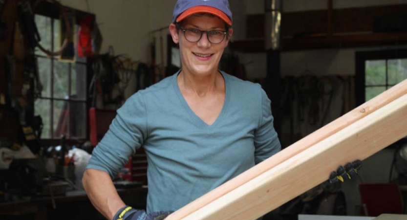 A person smiles at the camera while holding a piece of wood during a service project with Outward Bound.